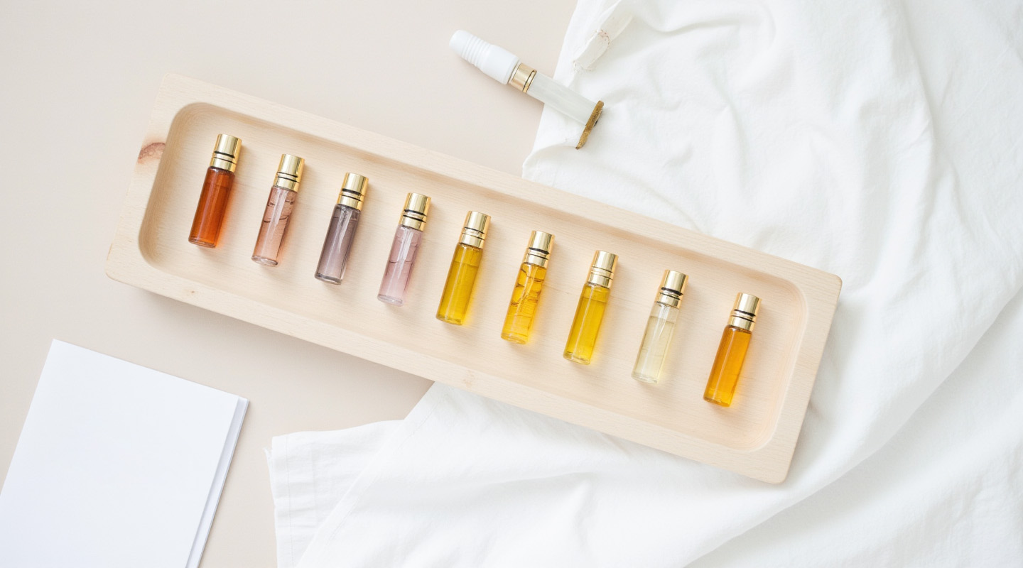 A flat lay of ten 2ml perfume oil sample vials on a wooden tray with a notebook and pen, representing a starter kit for entrepreneurs and DIY fragrance creators.