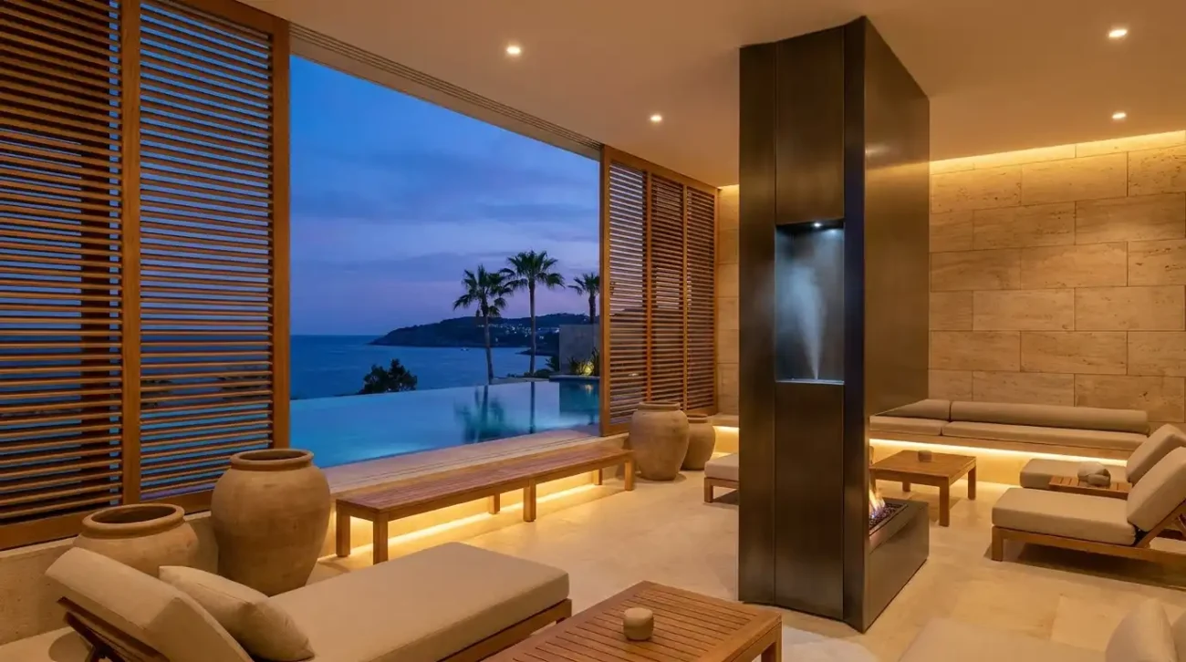 A minimalist outdoor wellness lounge with teak wood columns and an integrated commercial scent diffuser next to an infinity pool.